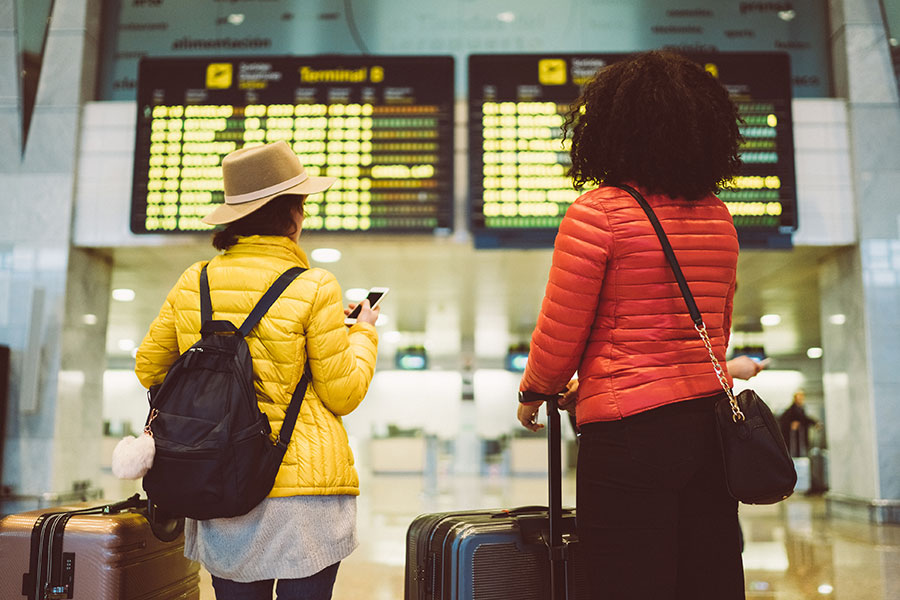 Two young female travellers look at an arrivals board in a station